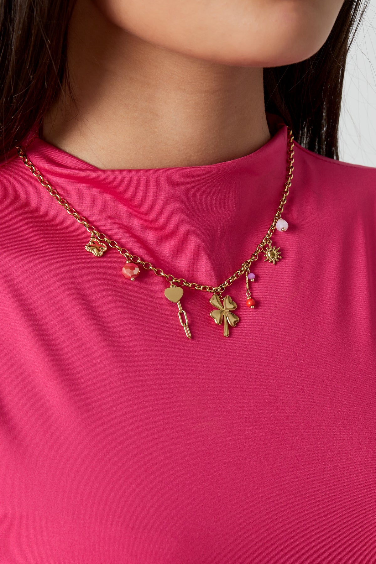 Collier breloques porte-bonheur doré trèfle cœur soleil porté sur tenue fuchsia